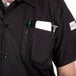A man wearing a Mercer Culinary Millennia black cook shirt with a pocket full of tools.