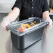 A person in gloves holding a Carlisle clear polycarbonate food pan lid with food inside.