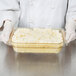 A person in a white coat holding a Cambro amber plastic food pan with mashed potatoes.