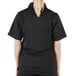 A woman wearing a Mercer Culinary black short sleeve cook shirt with full mesh back.