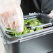 A person in a plastic glove reaching for a Carlisle Clear Polycarbonate Food Pan Lid on a container of salad.
