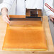 A person using a Matfer Bourgeat metal cake frame to cut a large cake.