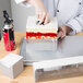 A person using a Matfer Bourgeat French square cake frame to insert a square cake.
