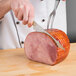 A hand uses a Mercer Culinary Renaissance® riveted fillet knife to slice ham on a wooden surface.