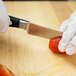 A person in white gloves using a Mercer Renaissance forged paring knife to cut a tomato.