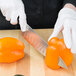 A person in white gloves cutting an orange bell pepper with a Mercer Culinary Renaissance chef's knife.