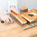 A hand using a Matfer Bourgeat French style cake frame to cut a square piece of cake.