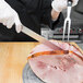 A person using a Mercer Culinary Renaissance serrated slicer to cut ham.
