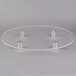 A clear circular Plexiglass cake stand on a table with silver objects on it.