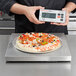 A person holding a Cardinal Detecto stainless steel pizza scale to display a pizza.