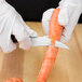 A person in white gloves using a Mercer Culinary Renaissance forged peeling knife to cut a carrot.