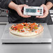 A person using a Cardinal Detecto stainless steel digital pizza scale to weigh a pizza.