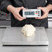 A person using a Cardinal Detecto stainless steel digital pizza scale to weigh white dough.