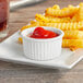 A plate of french fries with ketchup served in Acopa bright white fluted porcelain ramekins.