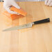 A person in gloves using a Mercer Culinary Z&#252;M&#174; fillet knife to cut a piece of salmon.