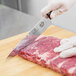 A hand in a glove using a Victorinox serrated chef knife to cut meat.