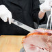 A person in a chef's uniform using a Victorinox rosewood carving knife to cut ham.
