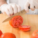 A person in a white glove using a Mercer Culinary Z&#252;M&#174; Forged Utility Knife to cut a tomato.