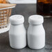 Two white ceramic bottle salt and pepper shakers on a table.
