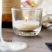 A Sterno PetiteLites glass candle on a table in a room with a glass of liquid.