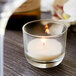 A Sterno PetiteLites clear wax filled glass candle on a table in a winery cellar.