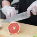 A person using a Victorinox chef knife to cut a grapefruit.