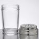 A clear glass cheese shaker with a stainless steel lid.