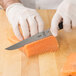 A person in a white glove using a Mercer Culinary Z&#252;M 6" Stiff Boning Knife to cut salmon.