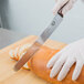 A person wearing gloves uses a Victorinox bread knife to cut a loaf of bread.