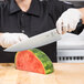 A person holding a Mercer Culinary chef knife and cutting a watermelon.