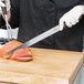 A person in a chef's uniform using a Victorinox Slicing/Carving Knife to cut meat.