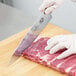 A person in gloves using a Victorinox chef knife to cut meat on a wooden cutting board.