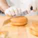 A person in white gloves using a Mercer Culinary bread knife to cut a bagel.