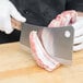A person in white gloves using a Victorinox curved meat cleaver to cut meat on a cutting board.