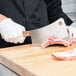A person using a Victorinox curved meat cleaver to cut meat on a cutting board.