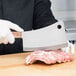 A person using a Victorinox curved meat cleaver to cut meat on a wooden surface.