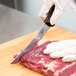 A person in gloves using a Victorinox curved boning knife to cut meat on a counter.