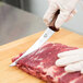 A person in gloves using a Victorinox narrow curved boning knife to cut meat.