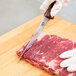 A person in gloves using a Victorinox narrow stiff boning knife to cut meat on a cutting board.