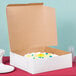 A white cake in a white 16" x 16" x 5" cardboard bakery box.