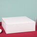 A white bakery box with a lid on a red table.