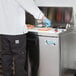 A person in a white coat and gloves making sandwiches on a counter with an Avantco 1 Door Refrigerated Sandwich Prep Table.