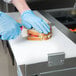 A person in blue gloves using a knife to cut a sandwich on an Avantco refrigerated prep table.