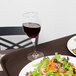 A Carlisle brown non-skid serving tray with a plate of salad and a glass of wine on a table.