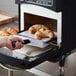 A hand using a black TurboChef aluminum paddle to put croissants in the oven.