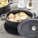An American Metalcraft pre-seasoned mini cast iron oval dutch oven with food in it and a lid.