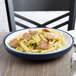 A dark blue Dinex Insul-Base meal delivery base with a plate of pasta with sausages and pesto on a table.