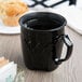 A black Dinex insulated mug with a handle on a table with a muffin.