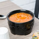 A bowl of soup in a Dinex Fenwick Onyx insulated bowl on a table.
