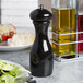 A Fletchers' Mill black pepper mill on a table next to a plate of salad.